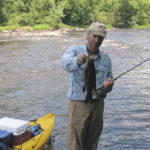 Tim Holschlag wade fishing beside his kayak, holding a big smallie