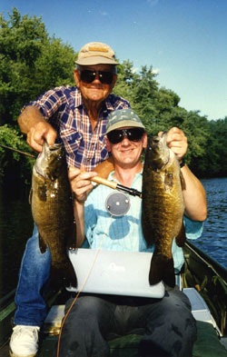 An angler and his father in the boat, each holding a big smallmouth bass.